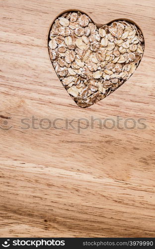 Dieting healthcare concept. Oat cereal oatmeal heart shaped on wooden surface. Healthy food for lowering cholesterol.