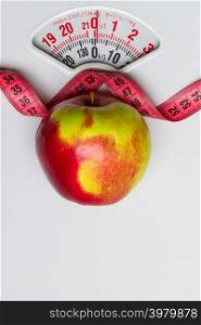 Dieting healthy eating slim down concept. Closeup apple with measuring tape on white weight scale