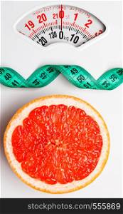 Dieting healthy eating slim down concept. Closeup grapefruit slice with measuring tape on white weight scale