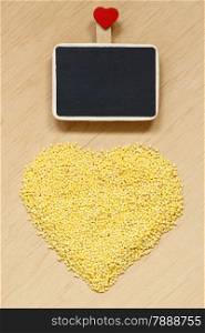 Dieting healthy food. Millet groats heart shaped and small blackboard board with space for text menu on wooden surface.