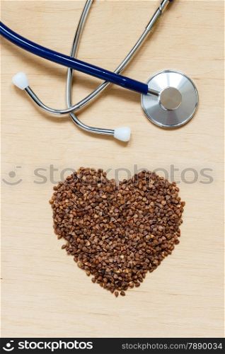 Dieting healthy living concept. Buckwheat groats heart shaped and stethoscope on wooden surface.. Healthy food good for cardiovascular system