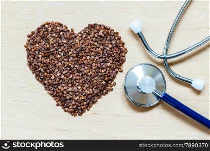 Dieting healthy living concept. Buckwheat groats heart shaped and stethoscope on wooden surface.. Healthy food good for cardiovascular system