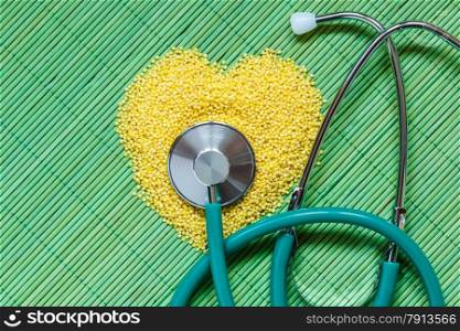 Dieting healthy living concept. Millet groats heart shaped and stethoscope on green mat surface.. Healthy food help lower cholesterol.
