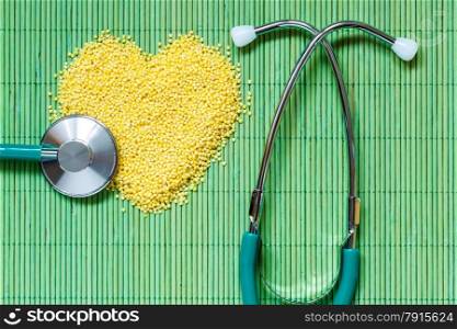 Dieting healthy living concept. Millet groats heart shaped and stethoscope on green mat surface.. Healthy food help lower cholesterol.