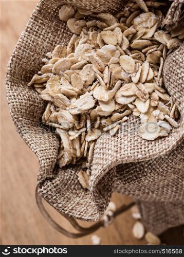 Dieting. Oat cereal in burlap sack on wooden surface, top, view. Healthy food for lowering cholesterol, protect heart.