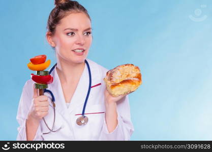 Dietitian nutritionist with sweet roll bun and vegetables like cucumber, tomato and pepper. Woman holding comparing junk and healthy food. Right eating nutrition concept.. Dietitian with sweet roll bun and vegetables.