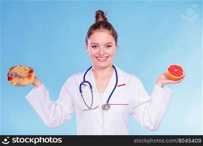 Dietitian with sweet roll bun and grapefruit.. Happy dietitian nutritionist with sweet roll bun and grapefruit. Woman holding fruit and cake comparing junk and healthy food. Right eating nutrition concept.