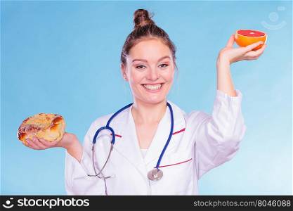 Dietitian with sweet roll bun and grapefruit.. Happy dietitian nutritionist with sweet roll bun and grapefruit. Woman holding fruit and cake comparing junk and healthy food. Right eating nutrition concept.