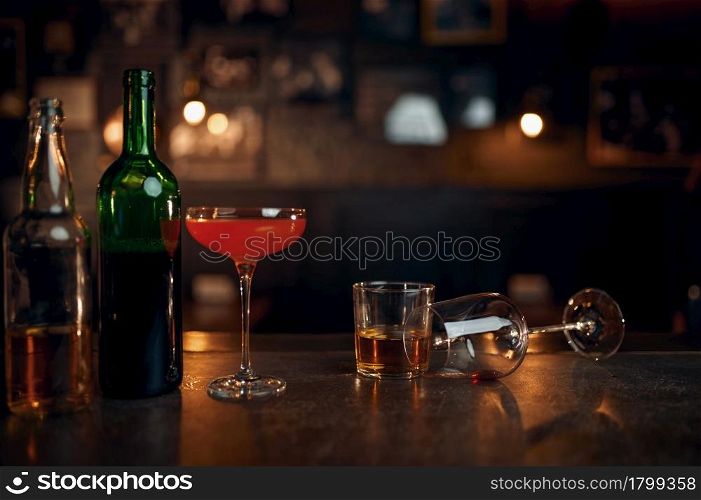 Different alcohol beverages on counter in bar, booze concept. Bottles and glasses on wooden table in pub closeup. Drinks assortment for stress relief or for fun. Different alcohol beverages on counter in bar