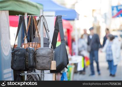 Different bags, purse and handbags on a flea market, people in the blurry background