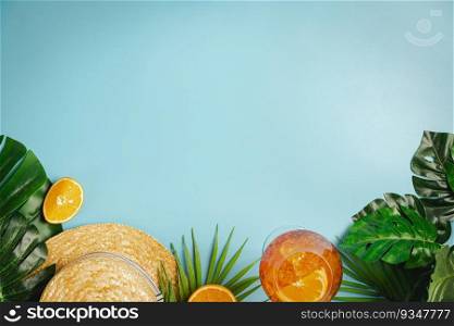 Different beach accessories, palm leaves, oranges and glass of aperol cocktail on blue background, top view, flat lay. Space for text. Summer beach background