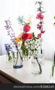 Different beautiful flowers in jars with water on the table near the window. Group of different flowers on the table