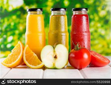 different bottles of juice with fruits on wooden table