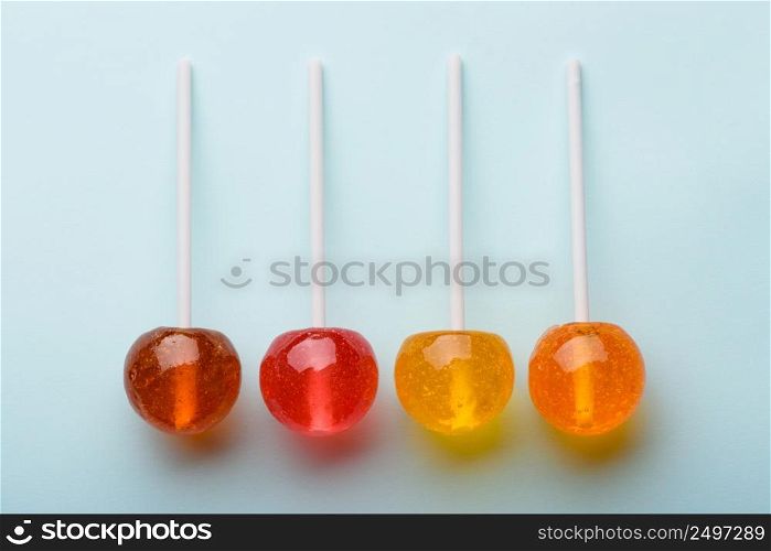 Different colored and flavoured big shiny lollipops on blue pastel background flatlay top view with shadows