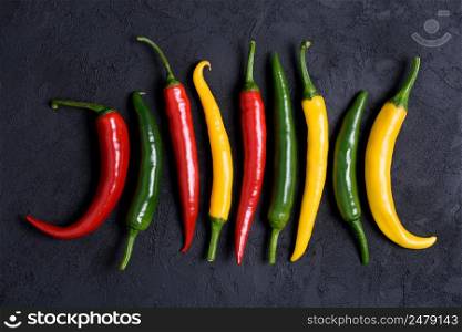 Different colored chili pepper on dark stone background
