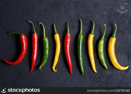 Different colored chilli peppers on dark background