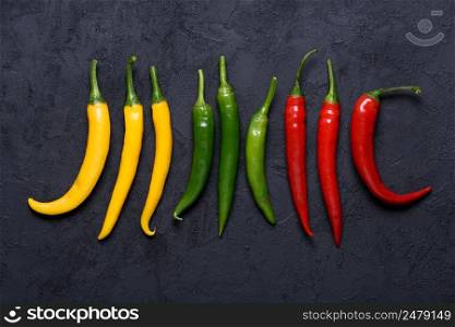 Different colored chilli peppers sorted by color on dark stone background