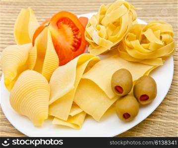 Different dry pasta with olives and tomat on a plate