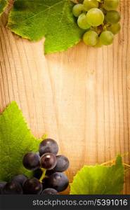 Different grapes with green leaves on wooden table