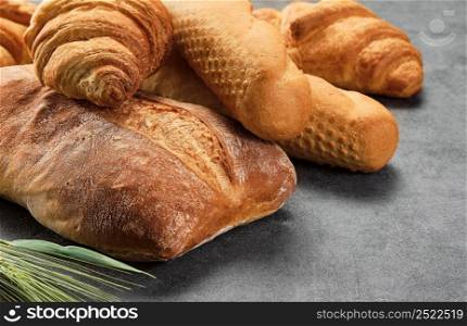 Different kinds of bread rolls on gray board, closeup. Kitchen or poster design for a local bakery. Baguette, croissant and ciabatta - various types of freshly baked bread