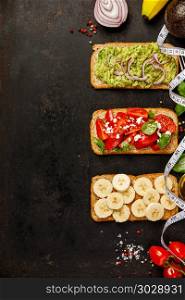 Different kinds of colorful whole grain bread sandwiches on dark background from above (top view). Clean eating, healthy, diet, weight loss food concept. Healthy sandwiches. Healthy sandwiches