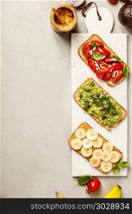 Different kinds of colorful whole grain bread sandwiches on white cutting board over grey concrete background from above (top view). Clean eating, healthy, diet, weight loss food concept. Healthy sandwiches. Healthy sandwiches