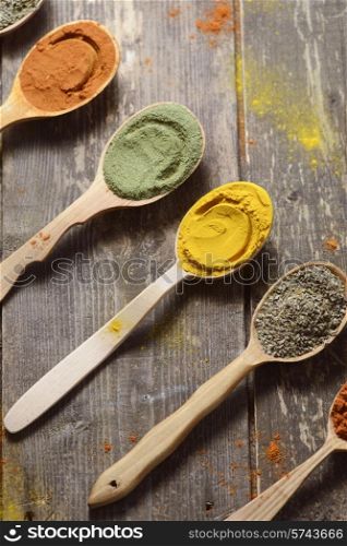 Different kinds of spices in wooden spoons on wooden background