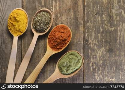 Different kinds of spices in wooden spoons on wooden background