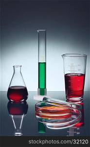Different laboratory glassware with color liquids on table with reflection