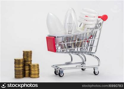 Different LED bulbs, energy-saving, incandescent are in the grocery cart, next to there are stacks of coins