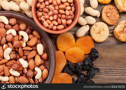 Different nuts in plates and dried fruits on a wooden background. Almond, hazelnut and peanut.