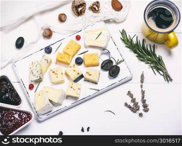 different pieces of cheese on a white wooden board and yellow cup with a coffee, top view