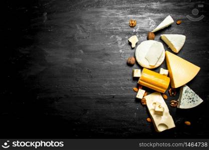 Different pieces of cheese with nuts. On a black wooden background.. Different pieces of cheese with nuts.