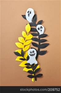 Different scary ghosts on paper branches leaves presented on a brown background with copy space. Paper handcraft composition to Halloween. Flat lay. Handcraft paper composition of yellow, black leaves and ghosts on a brown background with copy space for text. Halloween, Flat lay