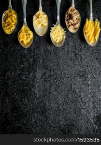 Different types of dry pasta in spoons. On black rustic background. Different types of dry pasta in spoons.