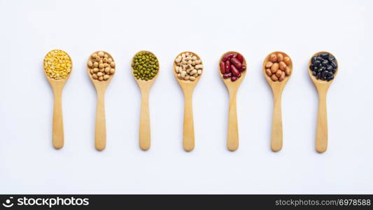 Different types of legumes on wooden spoon, white background.