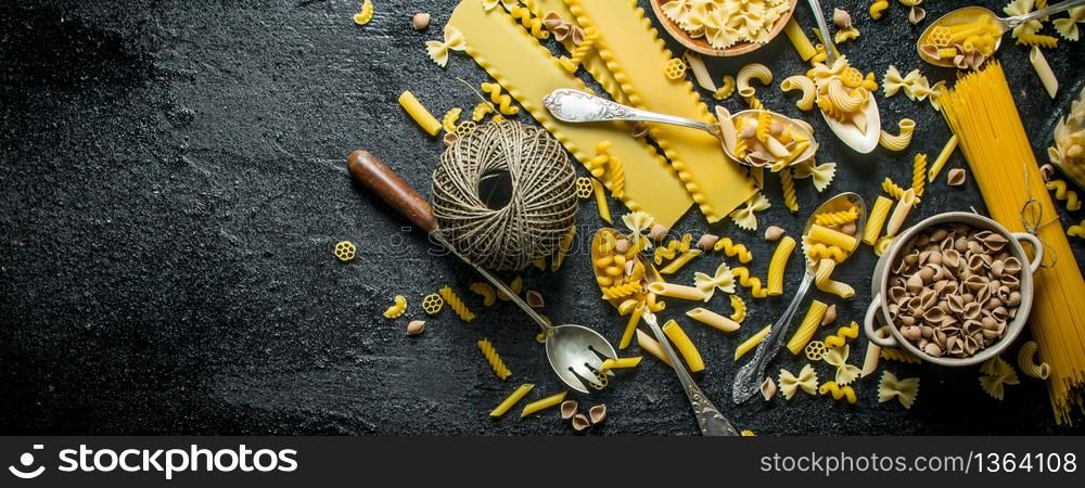 Different types of pasta dry the spoon and bowl. On black rustic background. Different types of pasta dry the spoon and bowl.