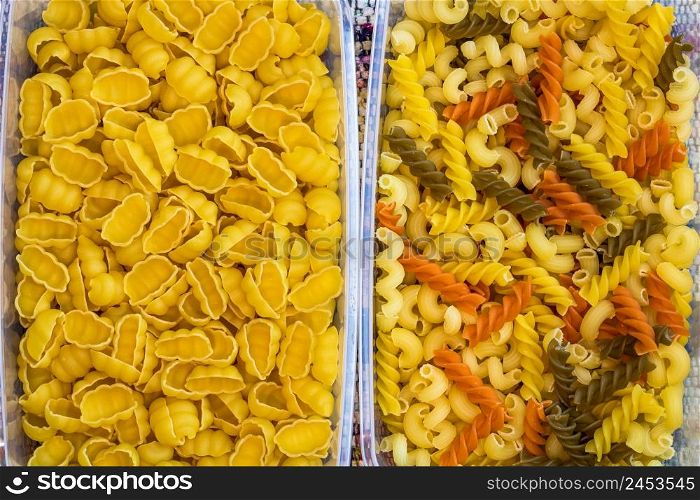 Different types of raw Italian pasta (gnocchi, tricolor pasta) in plastic transparent containers.. Different types of raw Italian pasta (gnocchi, tricolor pasta) in plastic transparent containers.