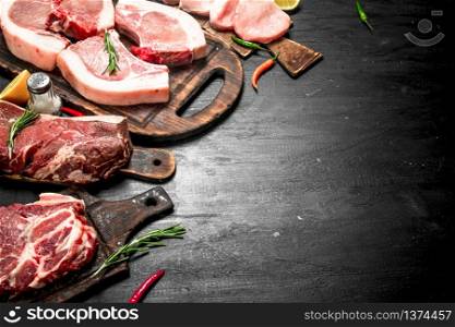 Different types of raw pork meat and beef with herb and spices. On the black chalkboard.. Different types of raw pork meat and beef with herb and spices.