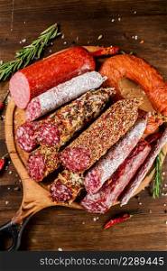 Different types of salami sausage on a wooden cutting board. On a wooden background. High quality photo. Different types of salami sausage on a wooden cutting board.