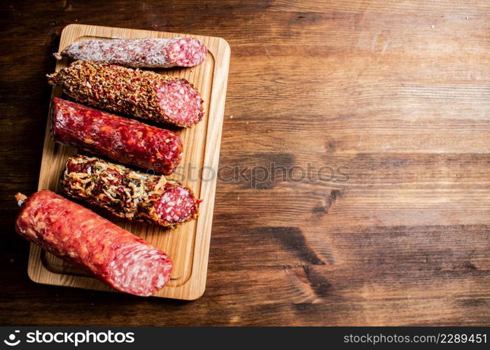 Different types of salami sausage on a wooden cutting board. On a wooden background. High quality photo. Different types of salami sausage on a wooden cutting board.