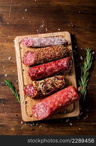 Different types of salami sausage on a wooden cutting board. On a wooden background. High quality photo. Different types of salami sausage on a wooden cutting board.