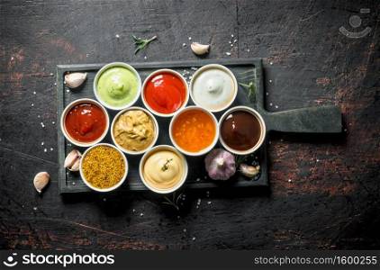 Different types of sauces in bowls on a cutting Board with garlic. On dark rustic background. Different types of sauces in bowls on a cutting Board with garlic.