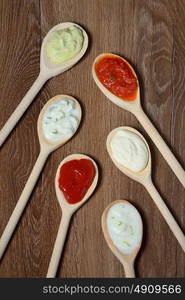 different types of sauces in spoons on wooden table