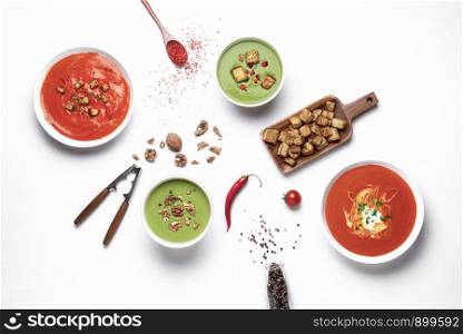 Different vegetable cream soups on white tabletop. Above view of green and red soups. Flat lay of healthy vegetarian meal. Spinach and tomato soups.