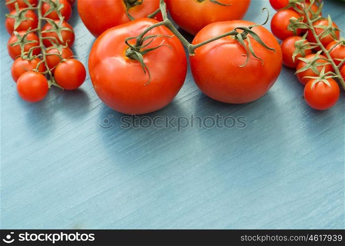 Differents size of tomatoes with leaf on a blue wooden surface