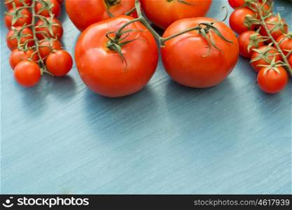 Differents size of tomatoes with leaf on a blue wooden surface