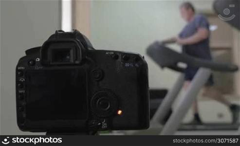 Digital camera shooting photos or timelapse of a man jogging on treadmill in the gym. Shot with changing focus