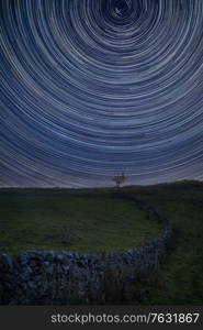 Digital composite image of star trails around Polaris with Beautiful Autumn Fall landscape countryside image of lone tree and stone wall