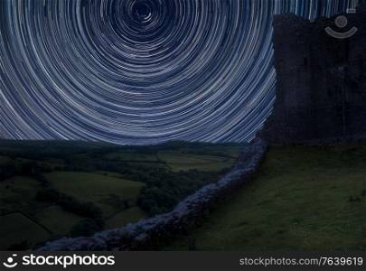 Digital composite image of star trails around Polaris with Beautiful image of medieval castle ruins in landscape with moody sky background